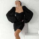 Woman in a black mini dress with puff sleeves leaning against a wall
