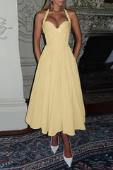 Woman wearing a pale yellow halter midi dress with a fitted bodice and full skirt.
