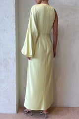 Back view of a woman in a pale yellow satin one-shoulder maxi dress, showing the sleek silhouette and the long asymmetrical sleeve.