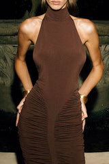 Back view of a woman in a brown ruched halter dress, highlighting the open back and ruched detailing.
