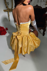 Woman wearing a yellow strapless satin dress with white opera gloves, back view showing lace-up detail and bow.