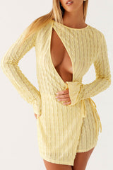 Front view of a woman wearing a light yellow textured mini dress with a plunging neckline and long sleeves, against a white background.