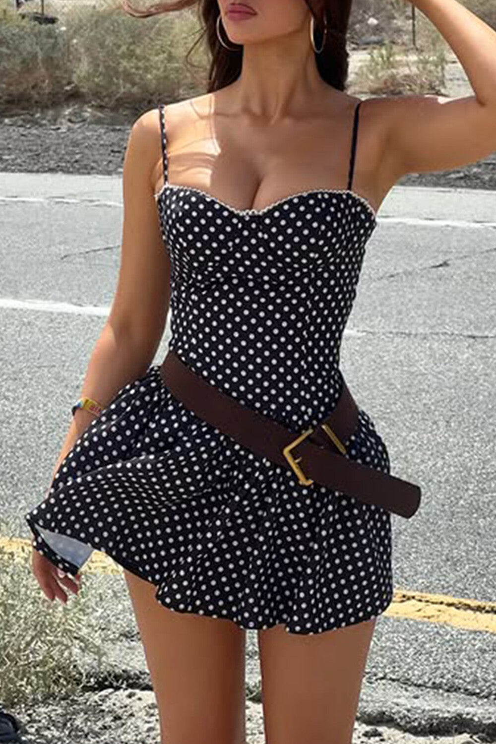 Woman posing in a polka dot mini dress with a brown belt.