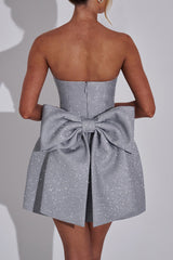Detail shot of the back of a silver glitter strapless dress, highlighting the voluminous bow and the fitted bodice.