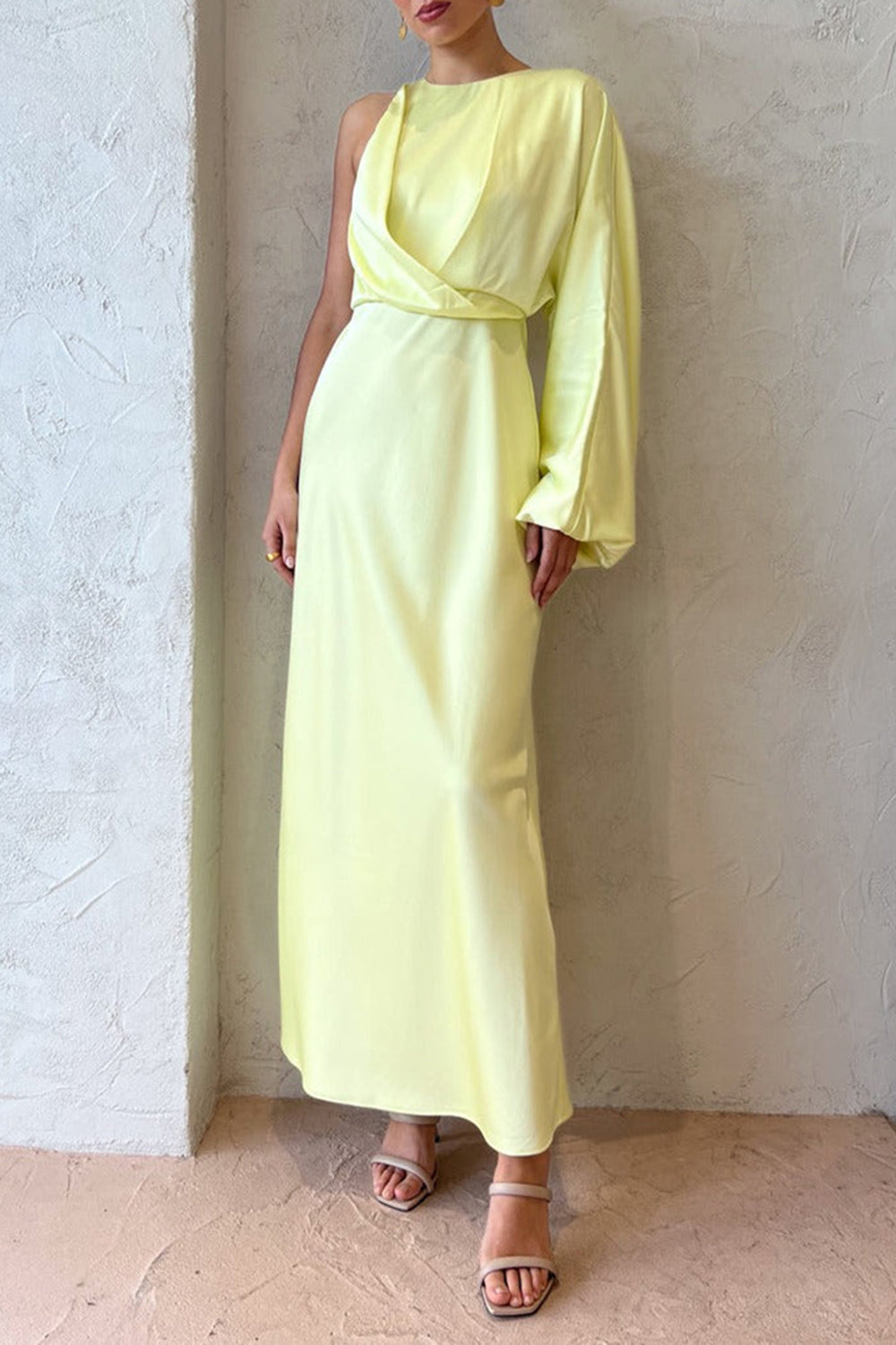 Full body shot of a woman in a pale yellow satin one-shoulder maxi dress, highlighting the flow of the skirt and the elegant design.