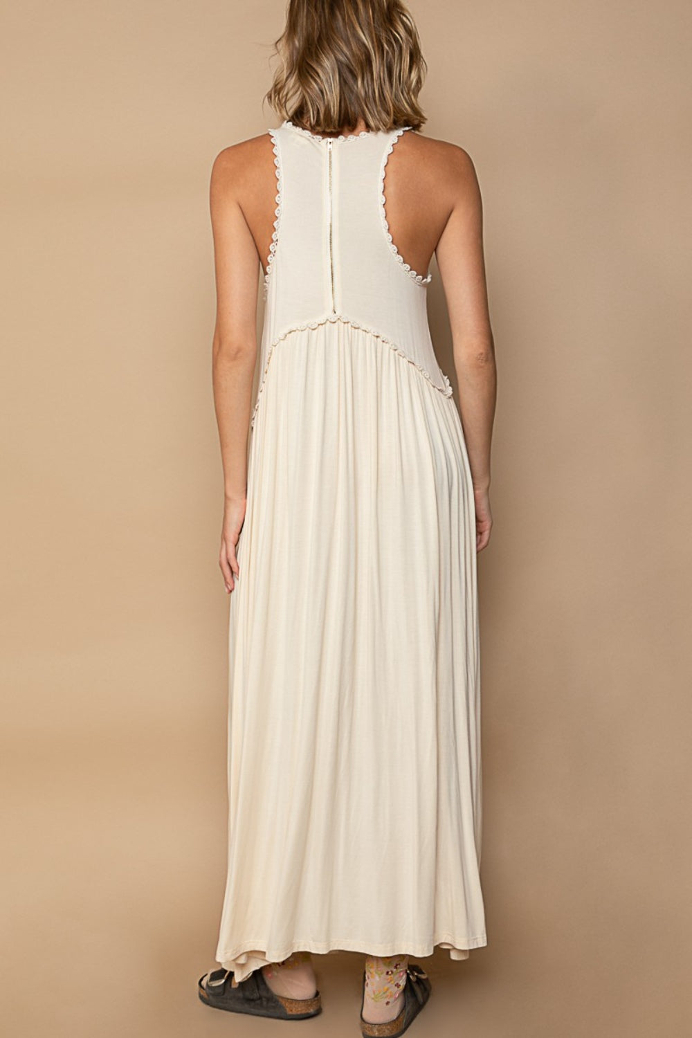 Back view of a woman in a cream-colored sleeveless maxi dress with a zipper closure