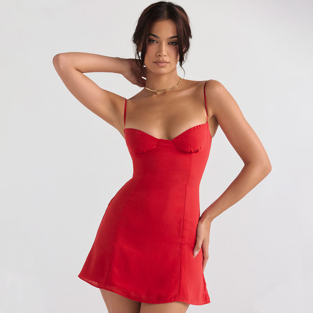 Woman in a red mini dress with spaghetti straps, touching her neck with one hand.