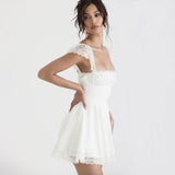 Woman in a white mini dress with lace trim, posing with hand on hip
