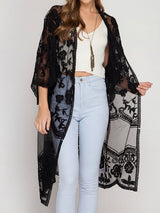 woman wearing a black lace kimono over a white crop top and light blue jeans
