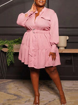 Plus-size woman wearing a long-sleeved, collared, belted mini dress with a tiered skirt in a pink color.