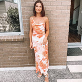 woman in orange and white tie-dye slip dress standing against a brick wall
