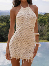 Woman wearing a cream crocheted halter dress with shell fringe standing by a pool