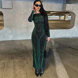 Woman wearing a black and green abstract print maxi dress with long sleeves, black sunglasses, and black boots, standing in a parking garage.