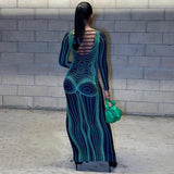 Back view of a woman wearing a black and green abstract print maxi dress with long sleeves and cut-out details on the back, holding a green handbag.