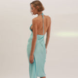 Rear view of a woman in a light blue satin slip dress with a low open back and halter tie closure.