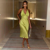 Woman wearing a lime green satin halter midi dress, standing in a hotel hallway and facing the camera.