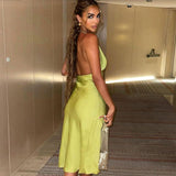 Woman wearing a lime green satin halter midi dress, standing in a hotel hallway and looking over her shoulder.