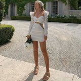 Full body shot of a woman wearing a white satin dress with cut-out details and embellished sides.