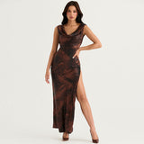 Woman wearing a brown and black abstract print satin maxi dress with a draped cowl neckline and a high slit on the left leg.