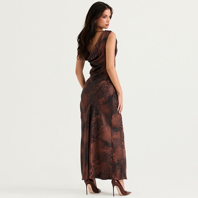 Rear view of a woman wearing a brown and black abstract print satin maxi dress with a draped cowl neckline and a high slit.
