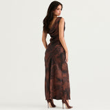 Rear view of a woman wearing a brown and black abstract print satin maxi dress with a draped cowl neckline and a high slit.