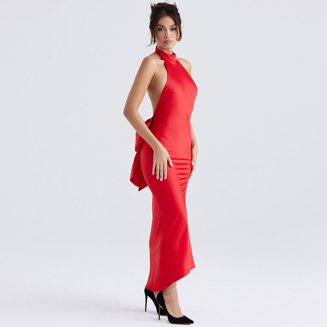 Side view of a woman in a red satin halter dress with a deep open back and a large bow detail.