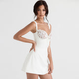 Woman wearing a white mini dress with lace detailing on the bust, posing with one hand on her hip