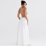 Woman wearing a white satin halter neck maxi dress with a high slit and open back, standing back view
