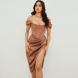 Full-body shot of a woman in a brown satin dress with an off-the-shoulder neckline and a high slit, posing with her hand on her hip.
