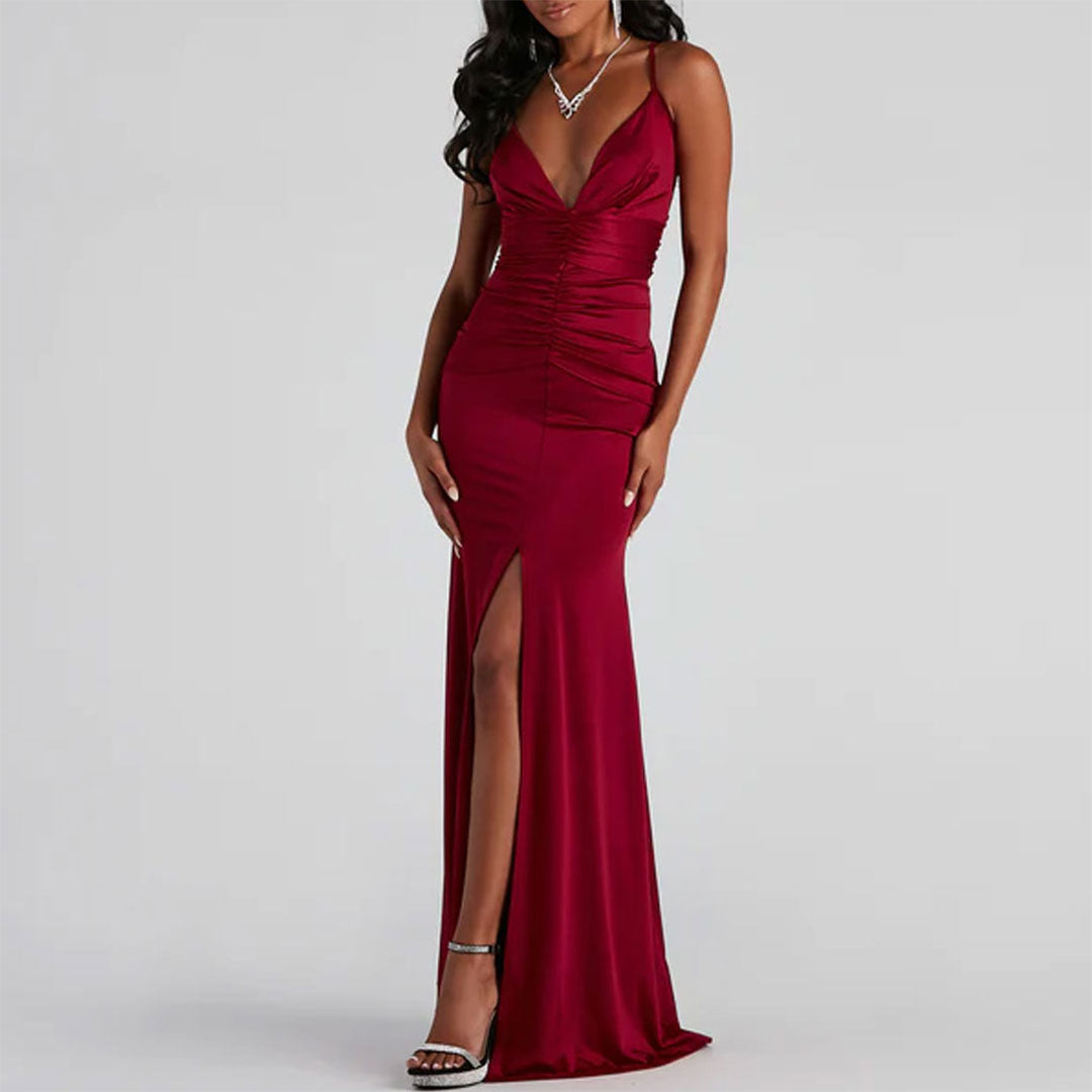 Woman wearing a floor-length, dark red satin dress with spaghetti straps and a high slit.