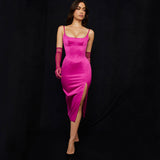 Woman posing in a bright pink satin dress with a high slit and spaghetti straps, wearing sheer pink gloves.