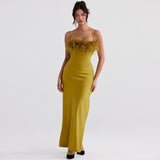 Woman wearing a yellow satin maxi dress with a feather trim bodice and spaghetti straps, standing against a white background.