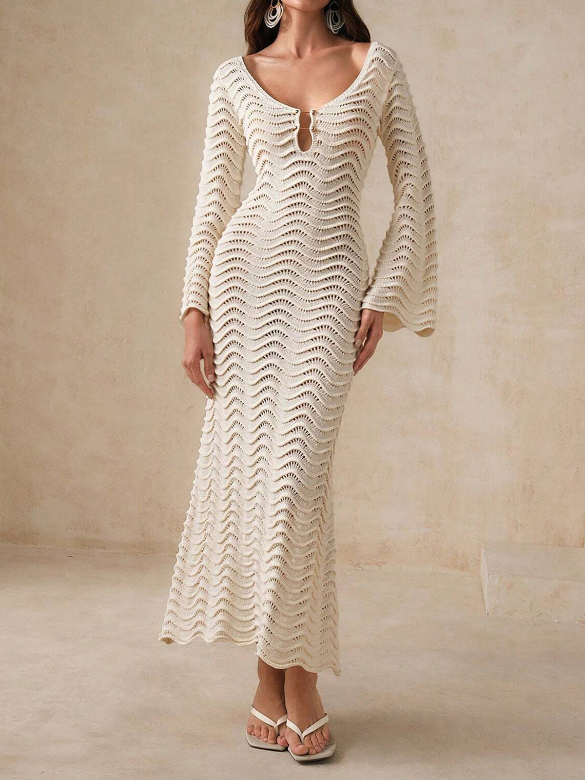 Woman wearing a cream-colored, long-sleeved, open-knit maxi dress with a wavy texture and bell sleeves.