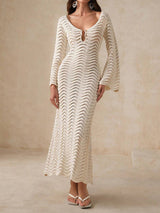 Woman wearing a cream-colored, long-sleeved, open-knit maxi dress with a wavy texture and bell sleeves.