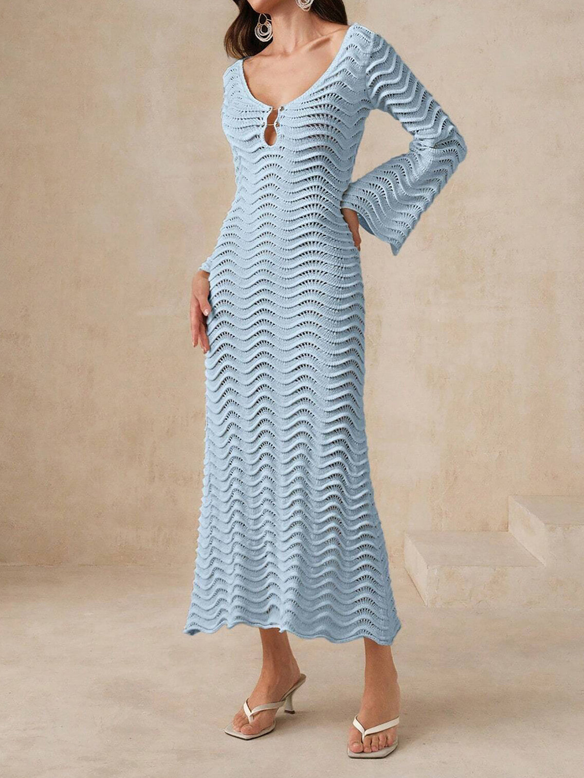 Woman wearing a light blue, long-sleeved, open-knit maxi dress with a wavy texture and bell sleeves.