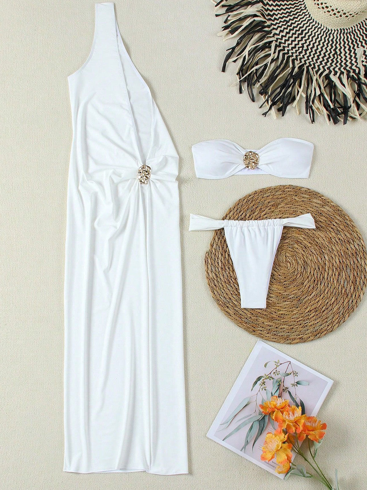 Flat lay of a white one-shoulder maxi dress, bikini top, bikini bottom, straw hat, and decorative items.