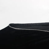 Detail shot of the embellished trim along the neckline of a black velvet dress.