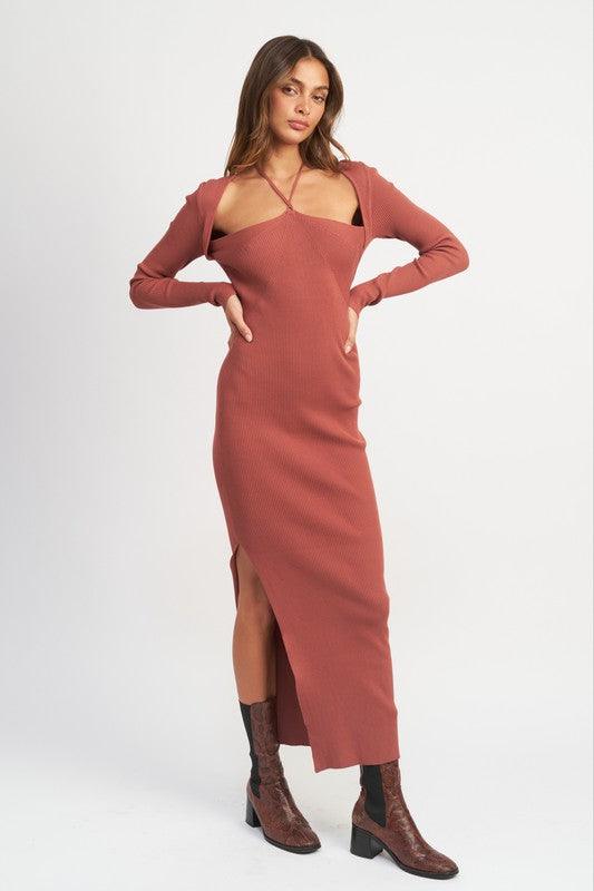 Woman wearing a terracotta ribbed knit maxi dress with a halter neckline and high slit, standing with hands on hips.