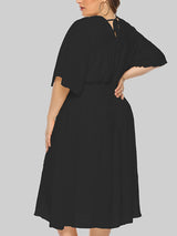 Plus-size woman wearing a black midi dress with flutter sleeves and a smocked waist, shown from the back.
