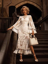 woman posing on stairs in a white lace dress with bell sleeves and fringe detail, holding a white handbag