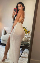 Woman wearing a white knit maxi dress with a high slit, posing for a mirror selfie from the back.