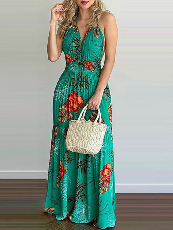 Woman wearing a green floral print maxi dress with a V-neck and halter neck, holding a small straw bag.