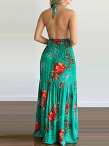 Back view of a woman wearing a green floral print maxi dress with a halter neck and open back.