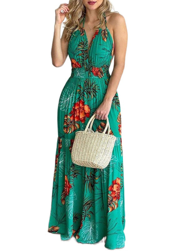 Woman wearing a green floral print maxi dress with a V-neck and halter neck, holding a small straw bag.