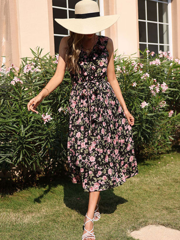 Woman in a black floral print midi dress and straw hat, posing outdoors