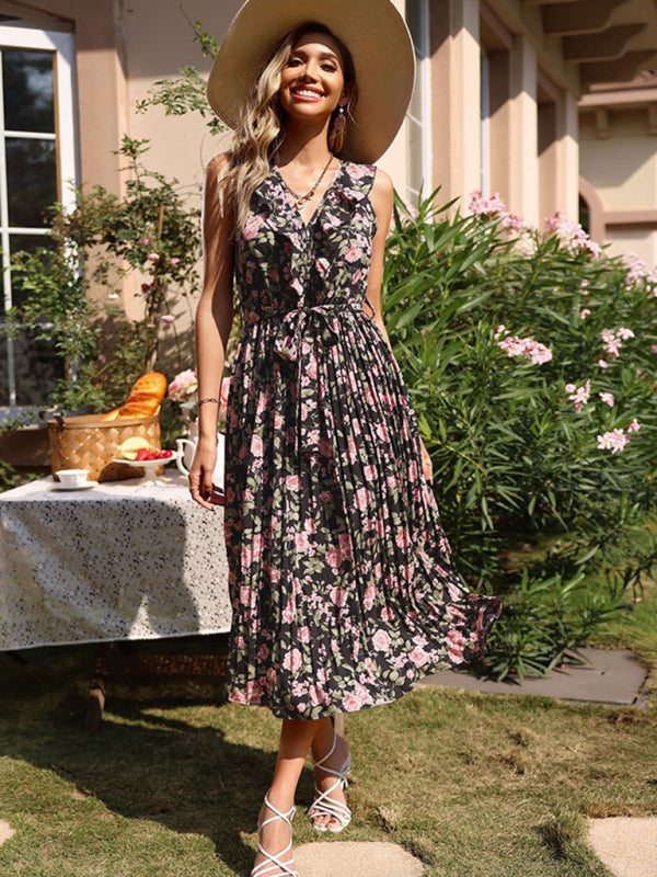 Woman in a black floral print midi dress and straw hat, standing outdoors with a picnic table in the background