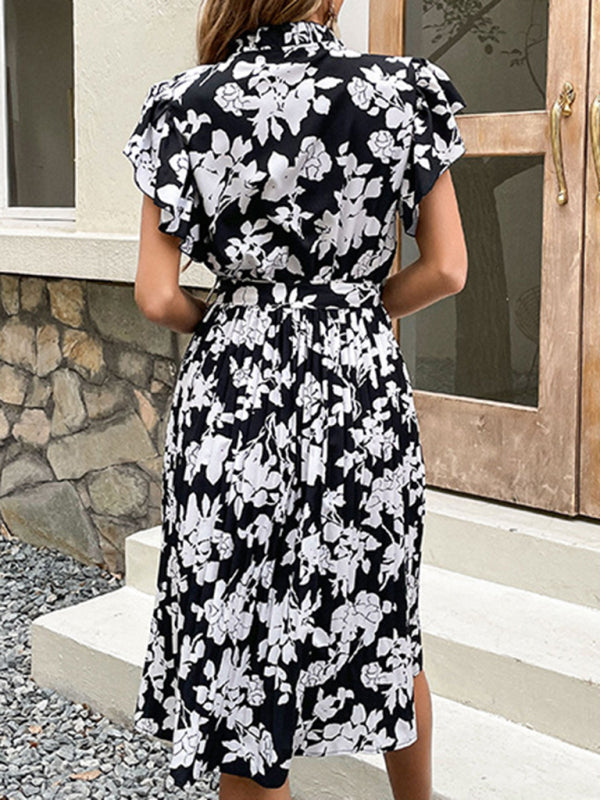 Rear view of a woman wearing a black and white floral print midi dress with a belted waist and pleated skirt.