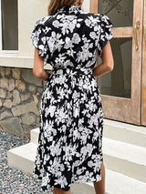 Rear view of a woman wearing a black and white floral print midi dress with a belted waist and pleated skirt.
