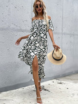 Woman in a floral print off-the-shoulder maxi dress holding a straw hat.