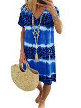 Woman wearing a blue tie-dye and leopard print short-sleeve V-neck A-line dress, holding a straw bag, with a white background.